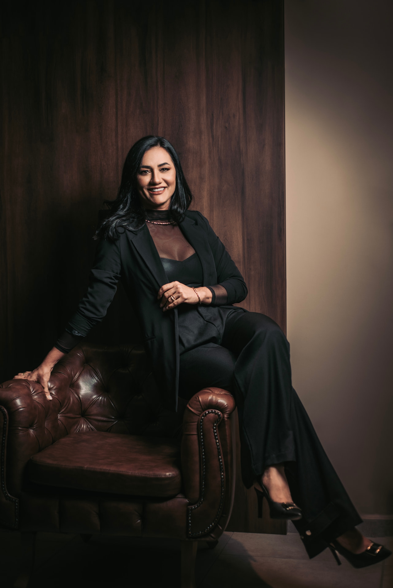 Márcia Canuto Abreu sentada em uma poltrona de couro, vestida de preto